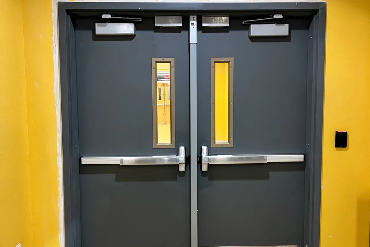 Commercial steel double doors with panic bar exit devices, door closers, and kick plates in a Washington DC building