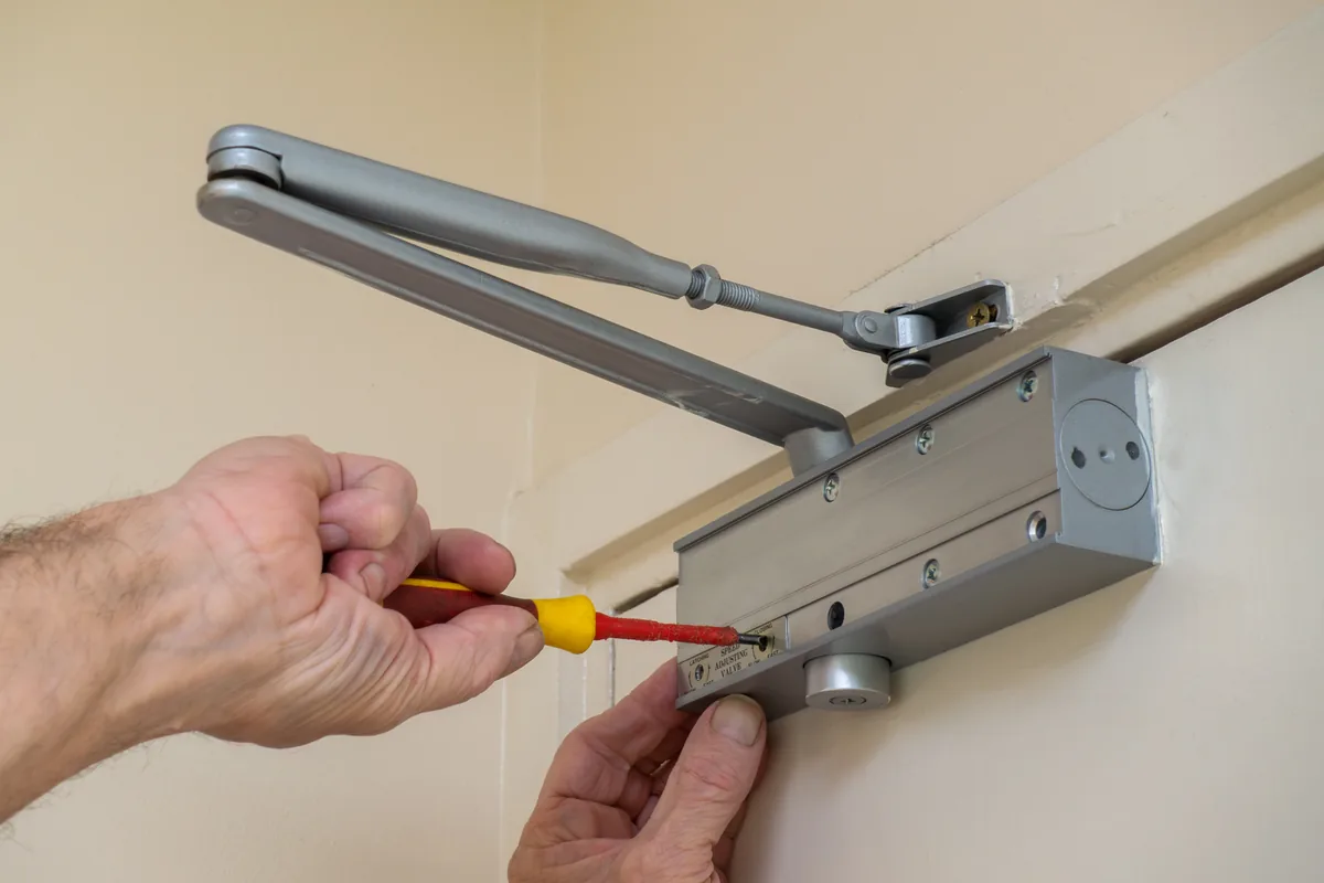 Technician adjusting the speed valve on a commercial door closer with a screwdriver, Washington DC door closer repair