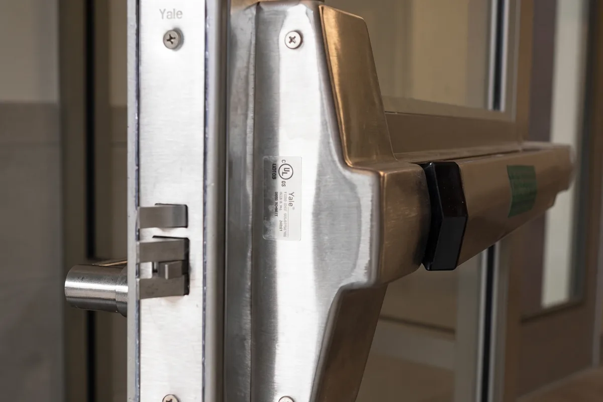 Close-up of a stainless steel panic bar (push bar) exit device and mortise latch on a commercial glass door in Washington, DC